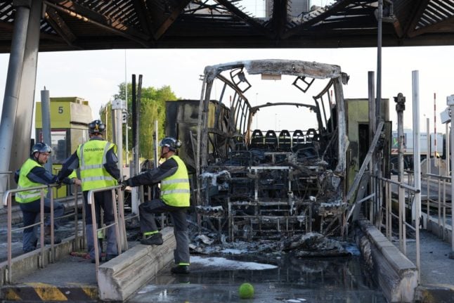 Tow-crew personnel stand by the charred remains of a bus as it sits at an A1 motorway toll in Fresnes-les-Montauban in northern France, after a clash occurred on the roadway between supporters of Paris Saint-Germain (PSG) and Olympique Lyonnais (OL) football teams en route to the French Cup football final