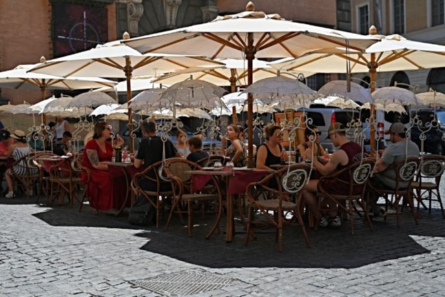 Diners sit in the shade of large parasols at a restaurant in central Rome