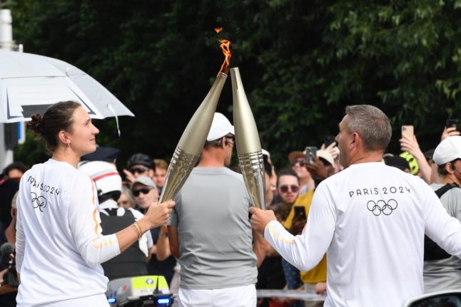 Former Olympic rower Inene Podpovitny passes the relay to another torchbearer in Strasbourg, north-east France, on June 26, 2024