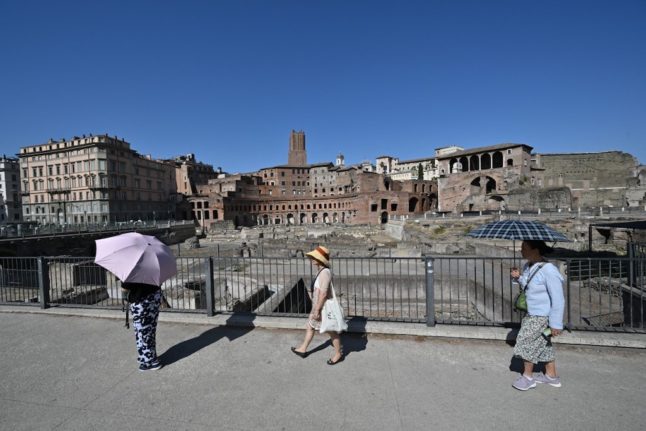 Tourist protect themselves with hats and umbrellas in front of Ancient Trajan's Markets in Rome.