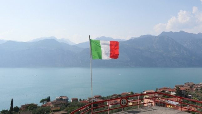 Italian flag waving in the wind with a lake in the background