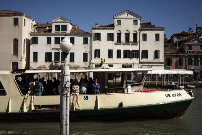 Tourists and residents stand on a water bus on the Grand Canal in Venice