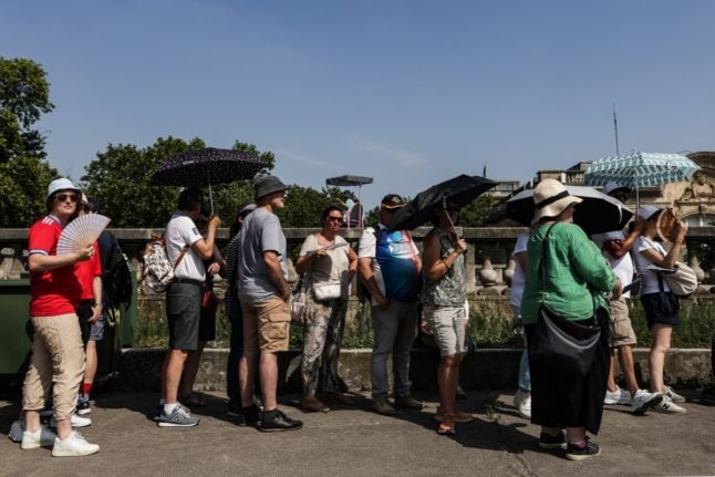 Pedestrians holding umbrellas for protection from the sun, wait in queue to watch an Olympic events in Paris