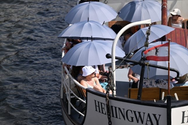 Visitors and tourists shelter from the sun beneath umbrellas on a boat tour on the Spree river during hot weather in Berlin, Germany,