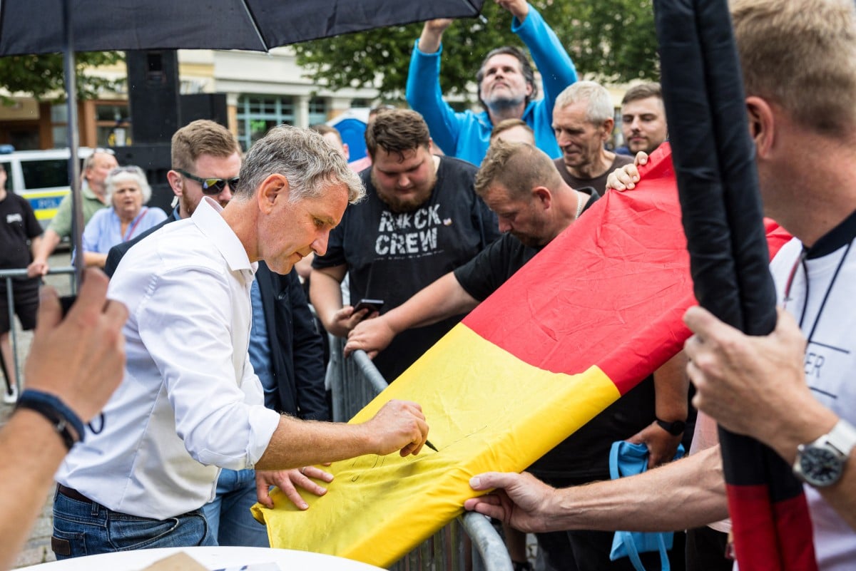 Björn Höcke, leader and top candidate of the far-right Alternative for Germany (AfD) party in the eastern German state of Thuringia, signs his autograph on a large German national flag belonging to supporters after addressing an election campaign event in Apolda, eastern Germany on August 18, 2024.