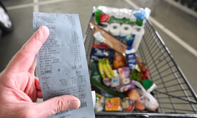 A person holds up a receipt and supermarket trolley.