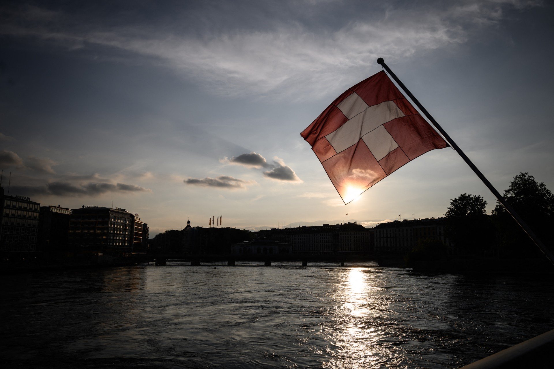 This picture taken on May 12, 2020, in Geneva, shows a Swiss flag above the Rhone river at sunset 