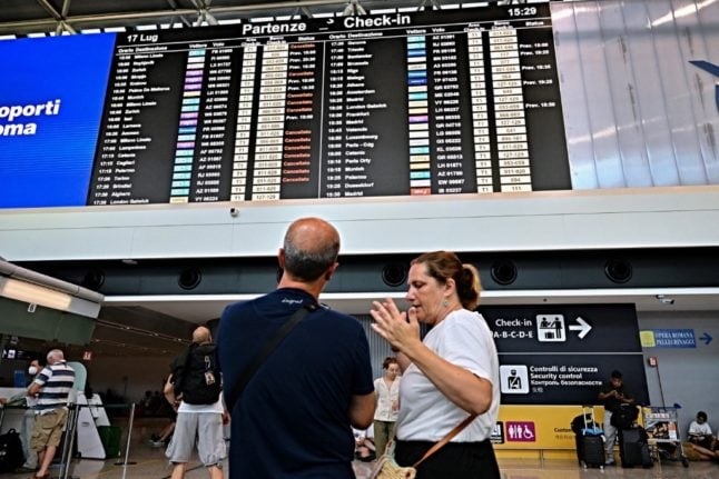 Passengers stand in front of a departure board at Rome Fiumicino airport