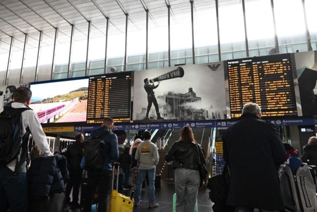 Commuters stand in front of a departure board at the Rome Termini railway station during a national strike