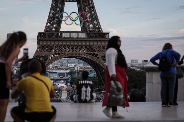 Pedestrians take pictures of the Olympic rings on the Eiffel Tower in Paris