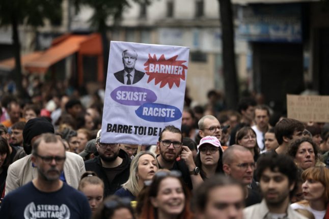 A protester holds a placard against newly appointed France's Prime Minister Michel Barnier during a rally to demonstrate against the French President's 