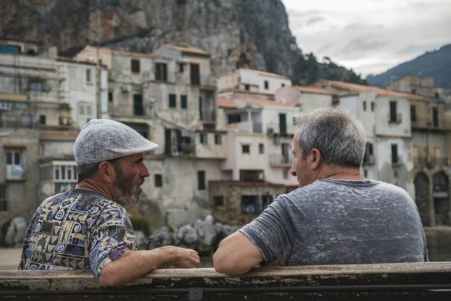 Two men sit on a bench in Cefalù, Sicily