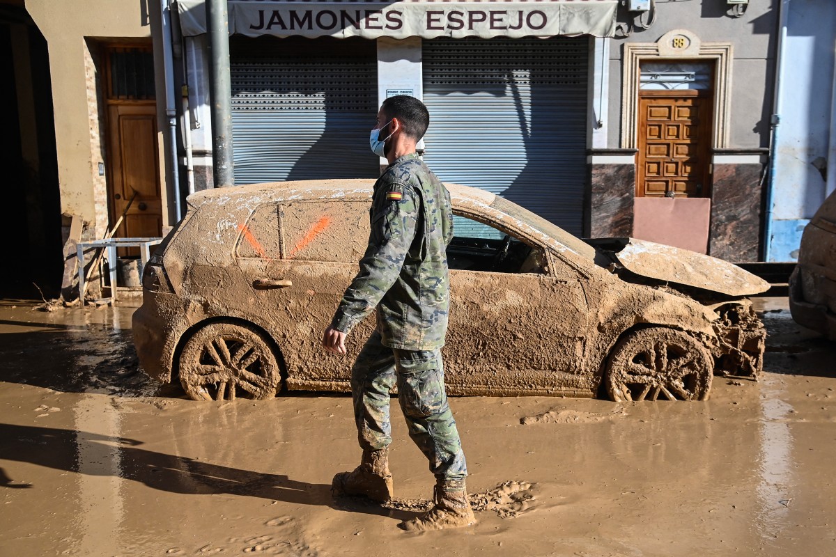 A soldier walks past a flood damaged car in Massanassa, in the region of Valencia, eastern Spain, on November 2, 2024, in the aftermath of devastating deadly floods