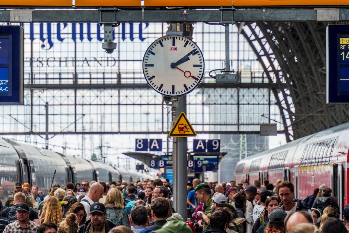 A large clock ticks away above a busy train station platform in Frankfurt.