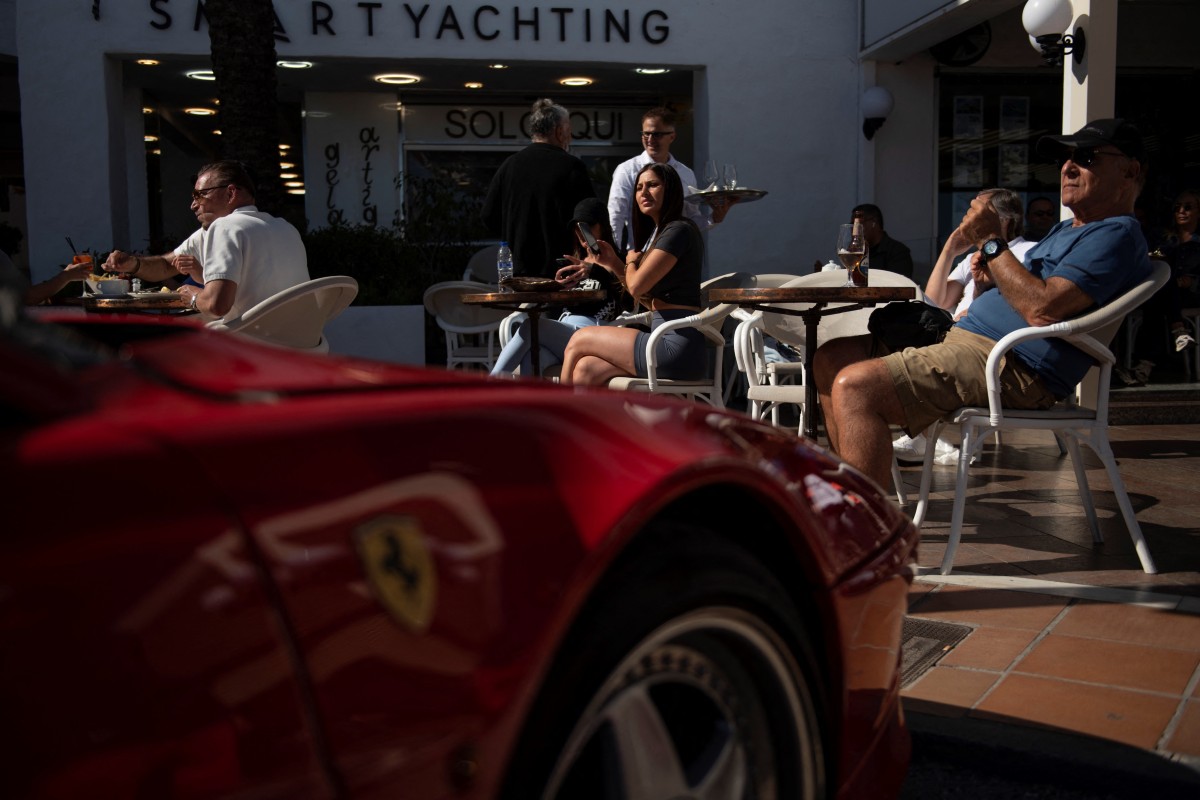 Customers sit at a terrace next to a Ferrari car in Puerto Banus luxury marina and shopping complex in Marbell