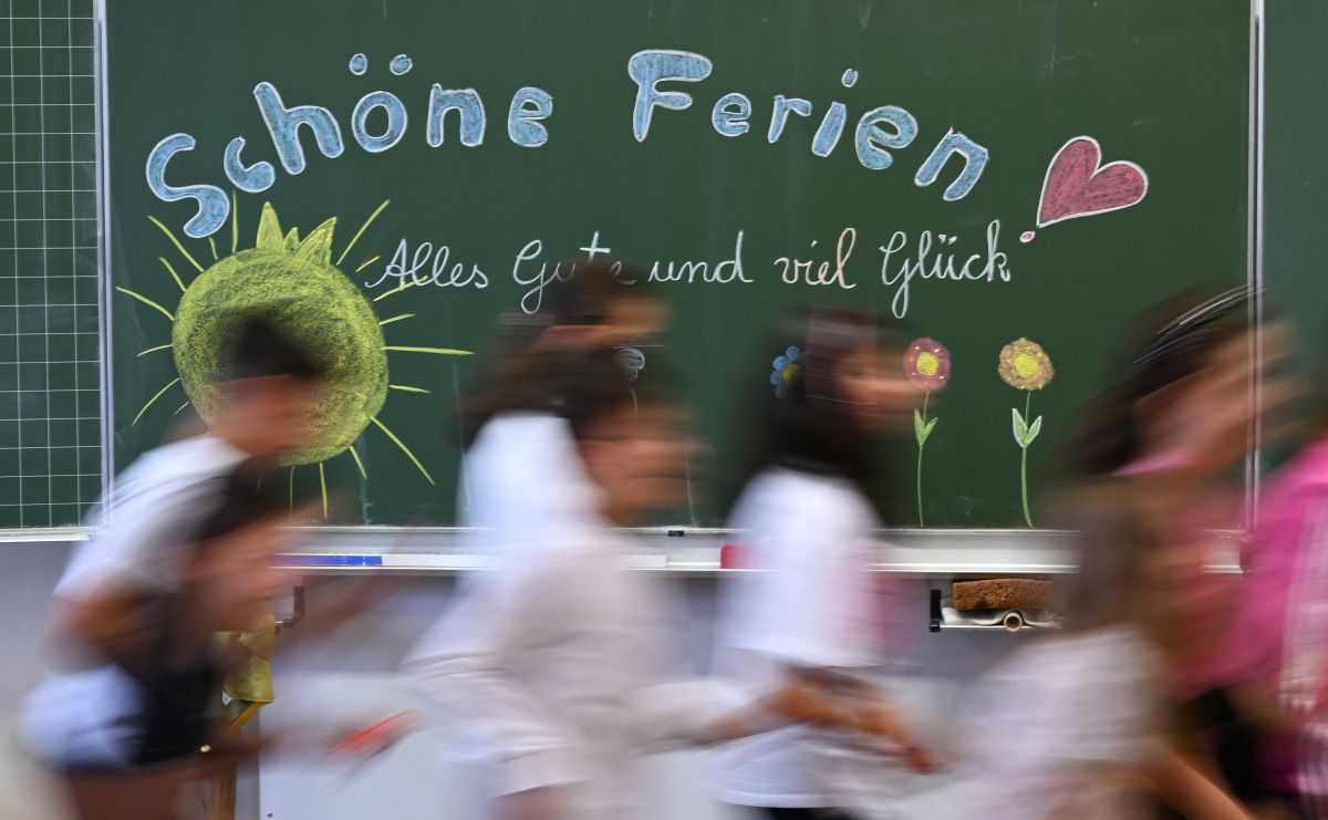 A blur of children run past a classroom chalkboard that reads 'Schone Ferien'.