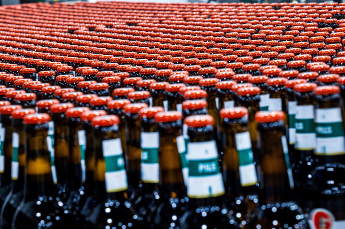 Hundresd of beer bottles are tightly packed together on a conveyer belt in a factory.
