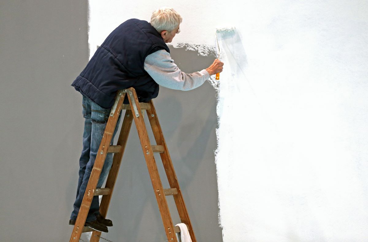 An elderly gentleman with gray hair whitewashes a wall