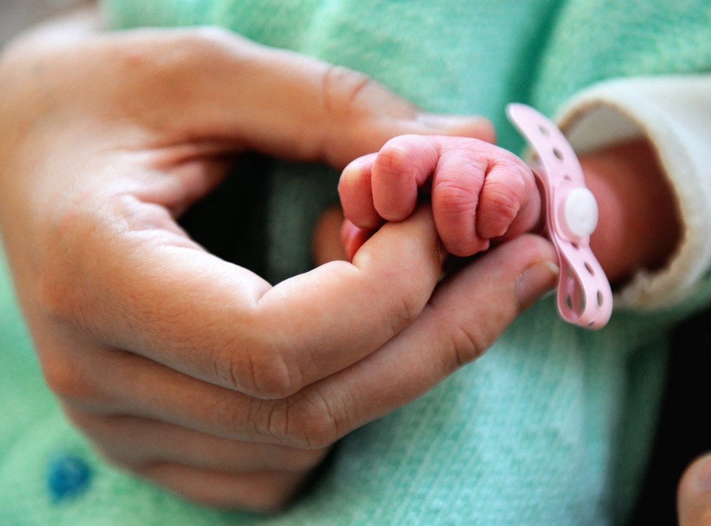 A newborn baby's hand is shown with its mothers.