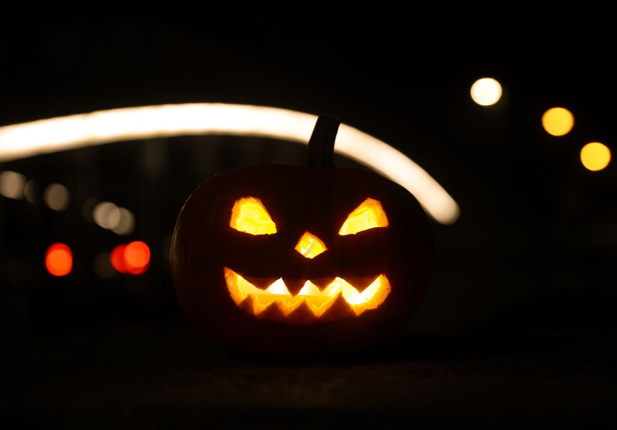 A hollowed-out pumpkin, illuminated and decorated with a face, stands on a lit bridge in the morning. 