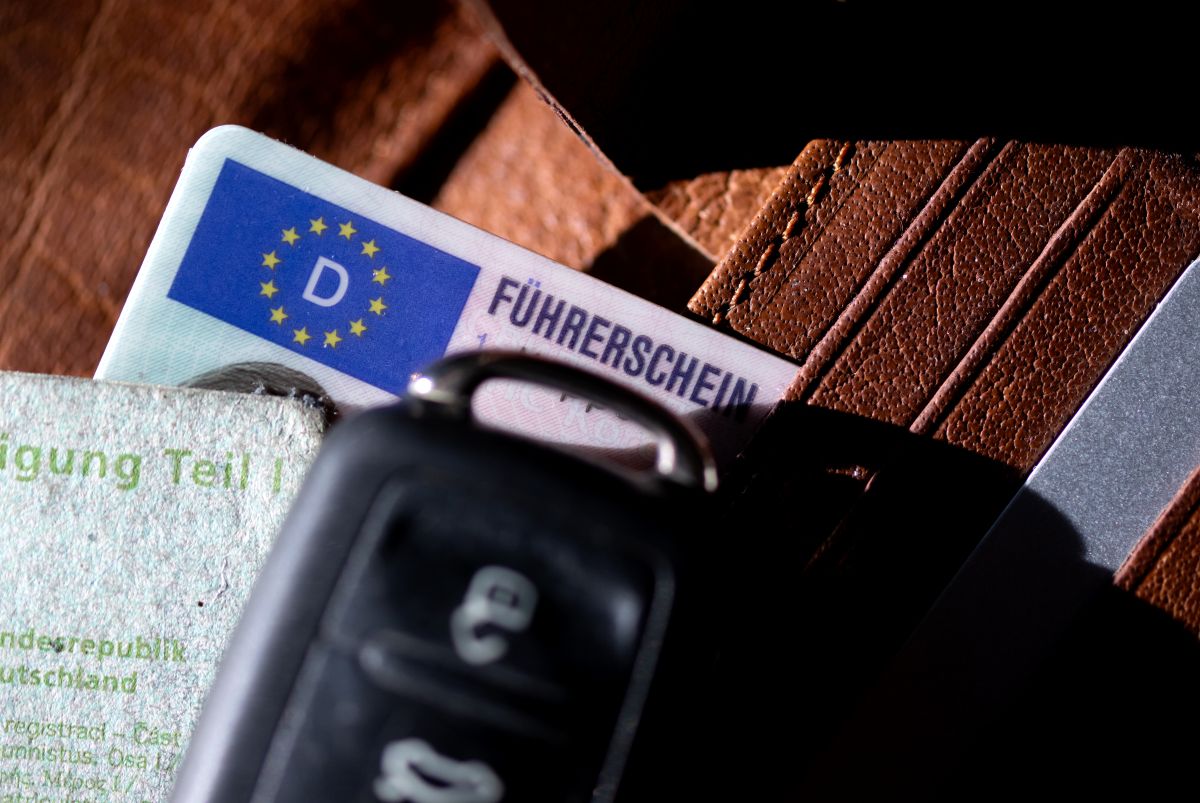 A driver's license, a car key and a registration certificate are on a wallet.
