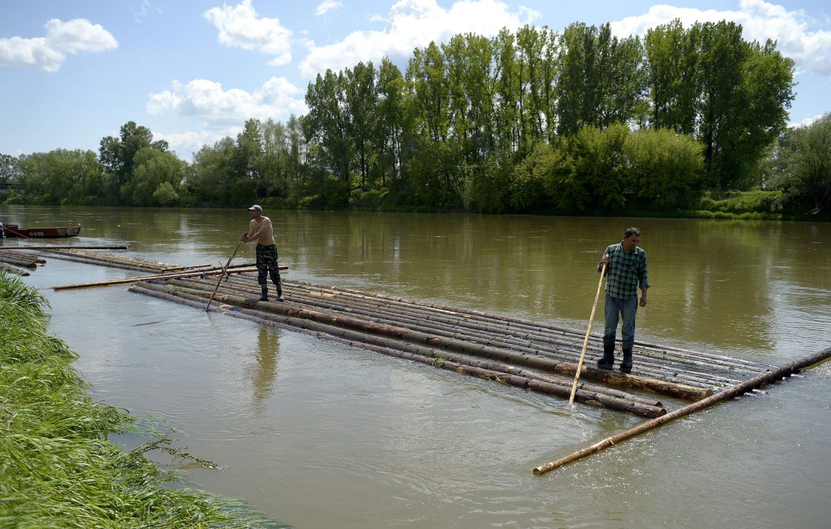 Two men stand on logs in a river in Poland