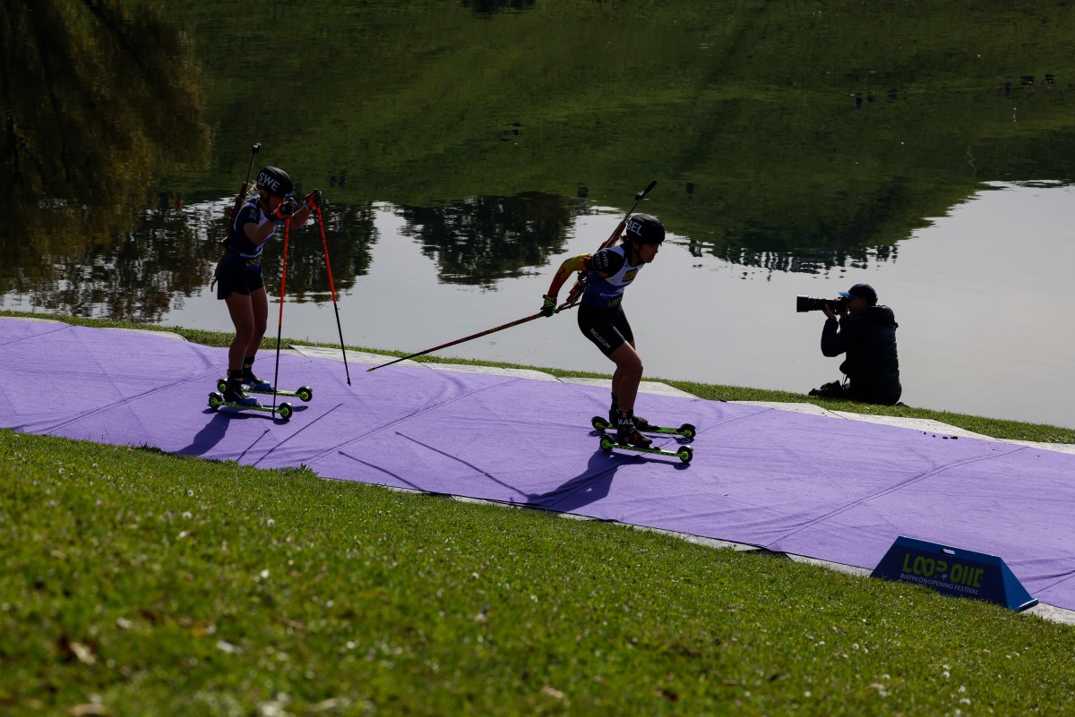 Biathletes on skates blur by a pond in Munich on a sunny day.