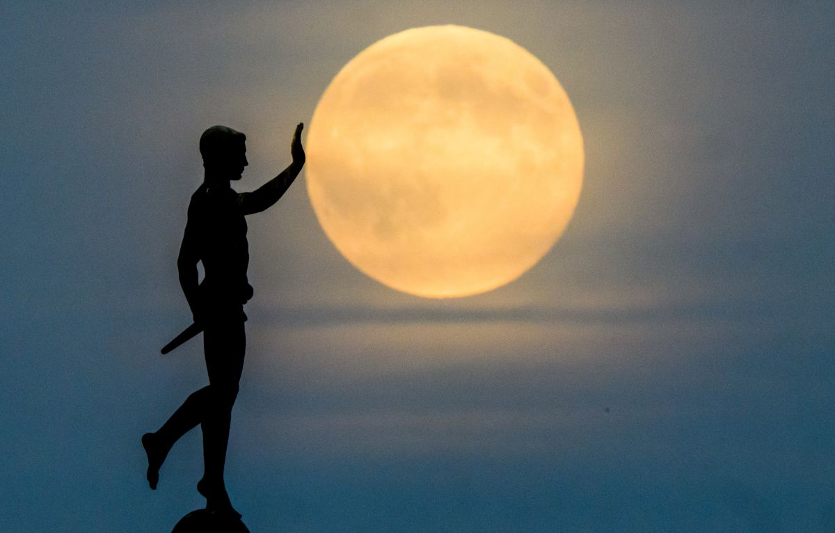 The silhouette of a man stands with a hand raised as if he's catching the large moon.
