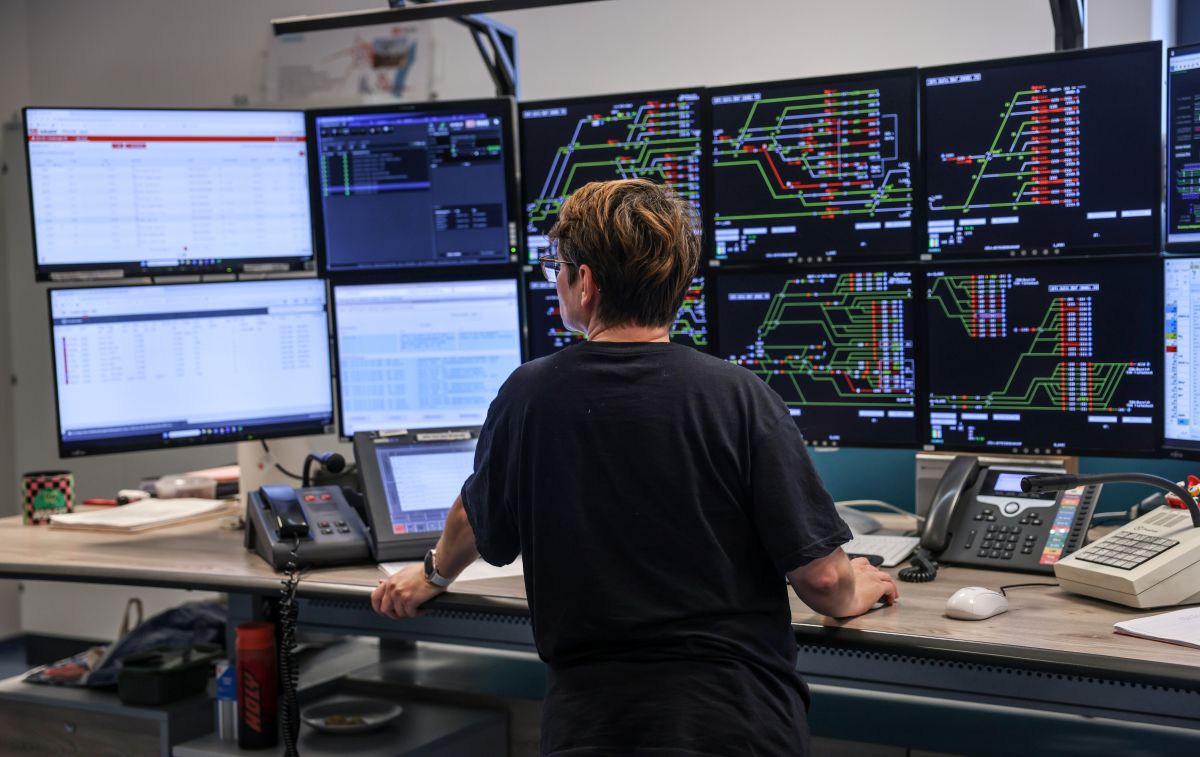 A woman looks at more than 10 screens which display train track switches in a DB control room.