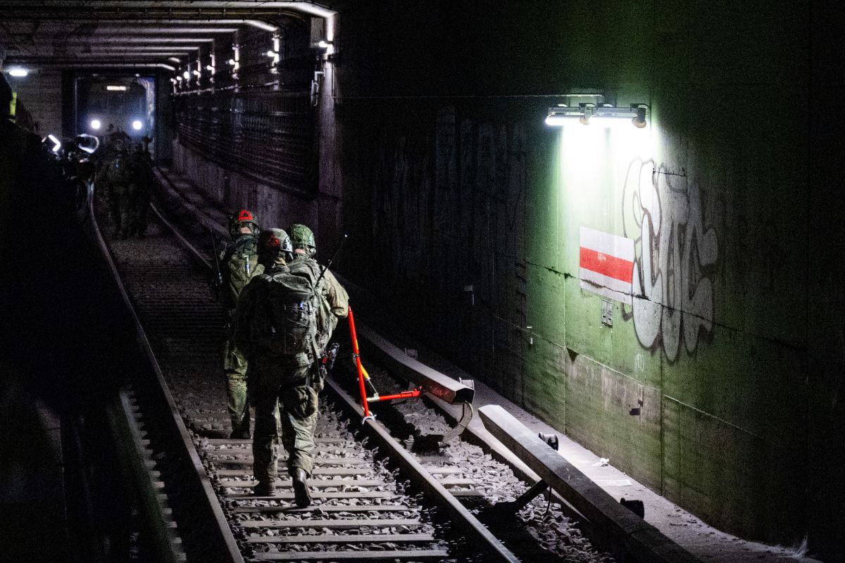Several soldiers are seen running down the train tracks in a dark tunnel toward a train.