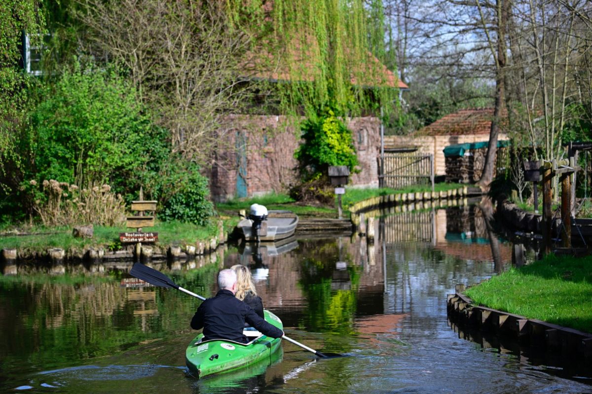 A man and woman in a green kayak paddle along the Spreewald canal.