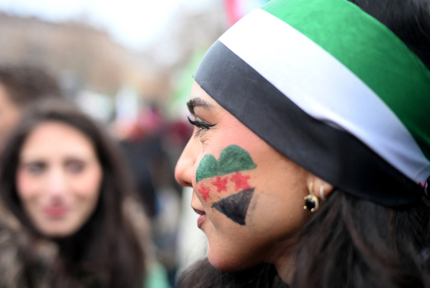 A member of the Syrian community has painted a heart in the colours of Syria on her cheek as she attends a rally on December 8, 2024 in Berlin.