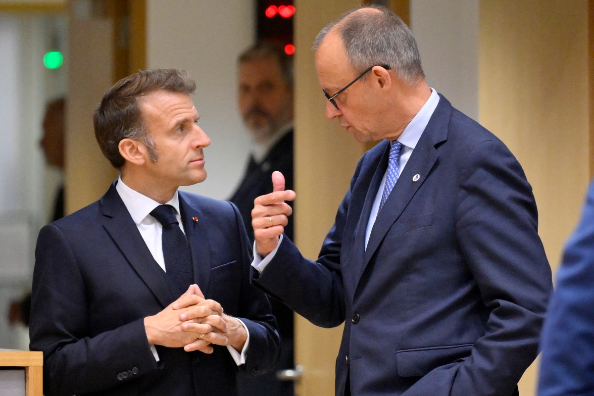 Mer makes a sign with his hand and MAcron holds his hands close to his chest as the two speak.