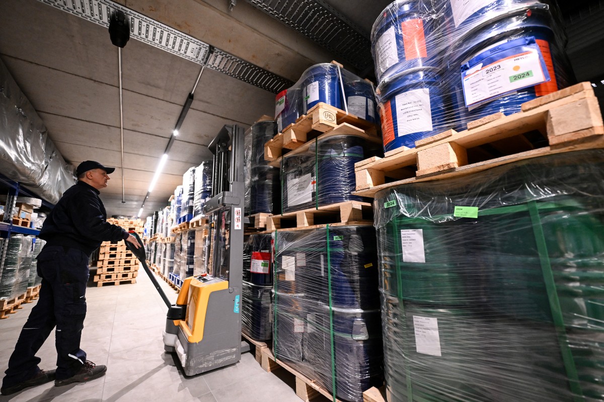 A man with a forklift is seen in a long hallway lines with large containers.