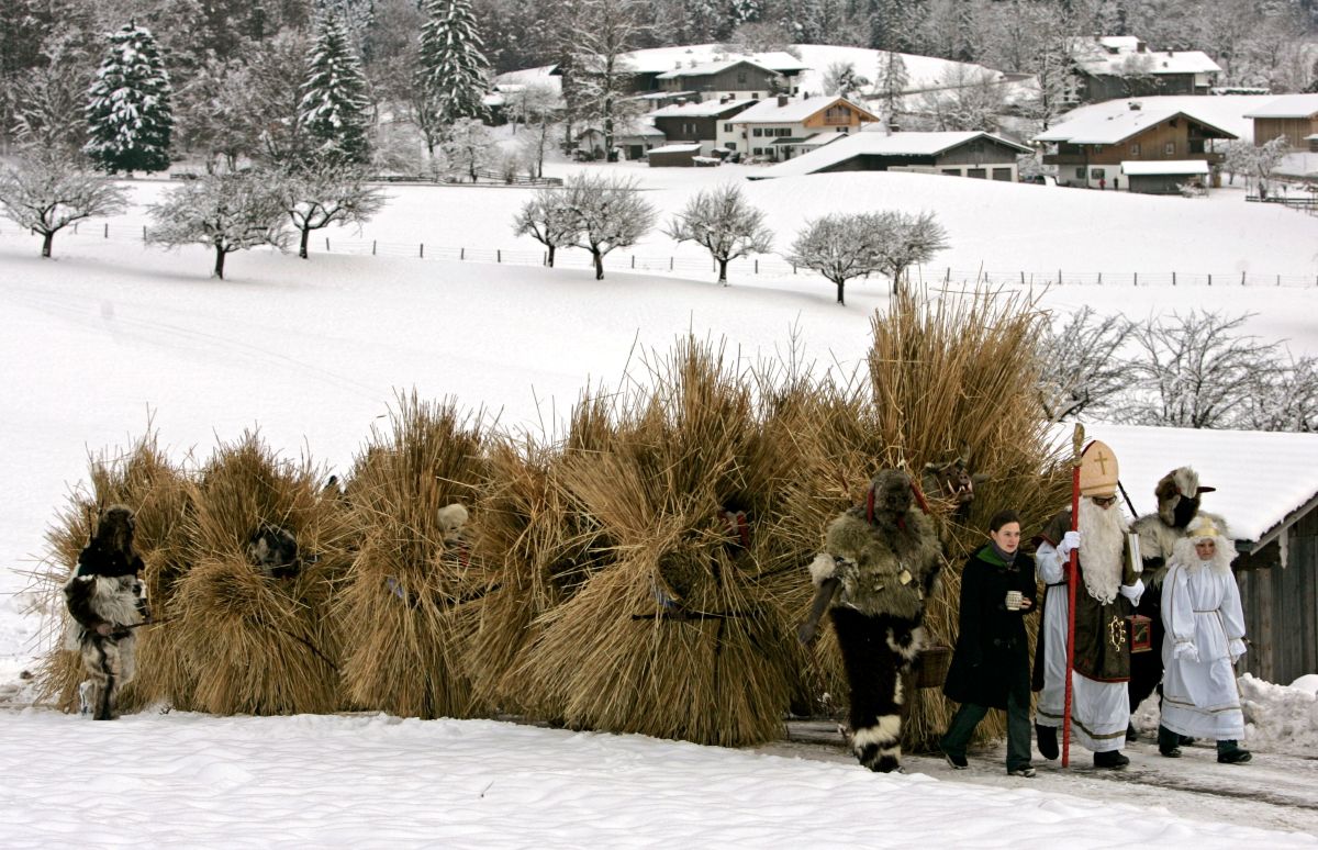 A parade of cretures covered in haw follow behind a Bishop in a fake beard.
