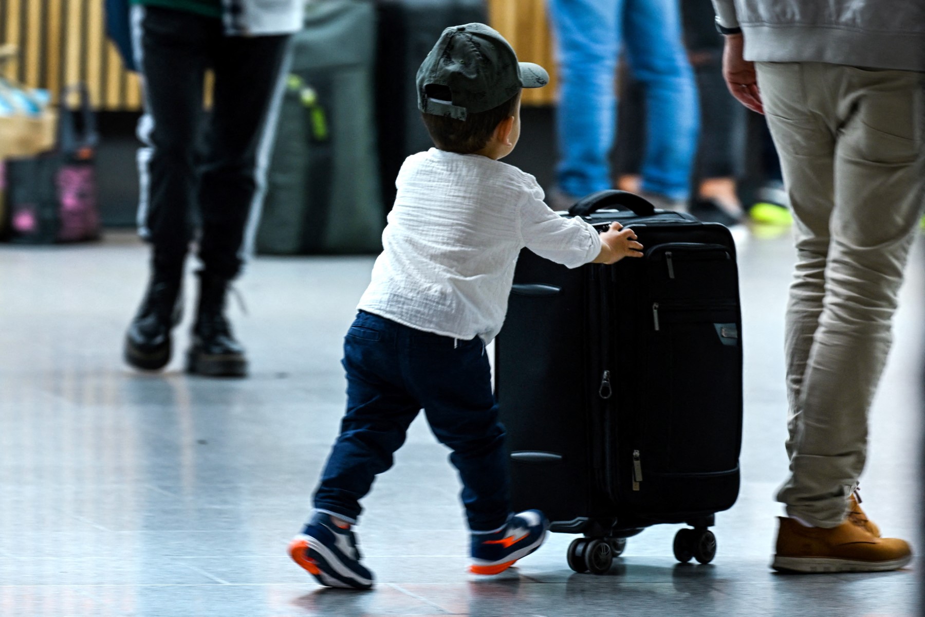 A boy pushes a bag that is talled than he is in the airport in Dusseldorf.