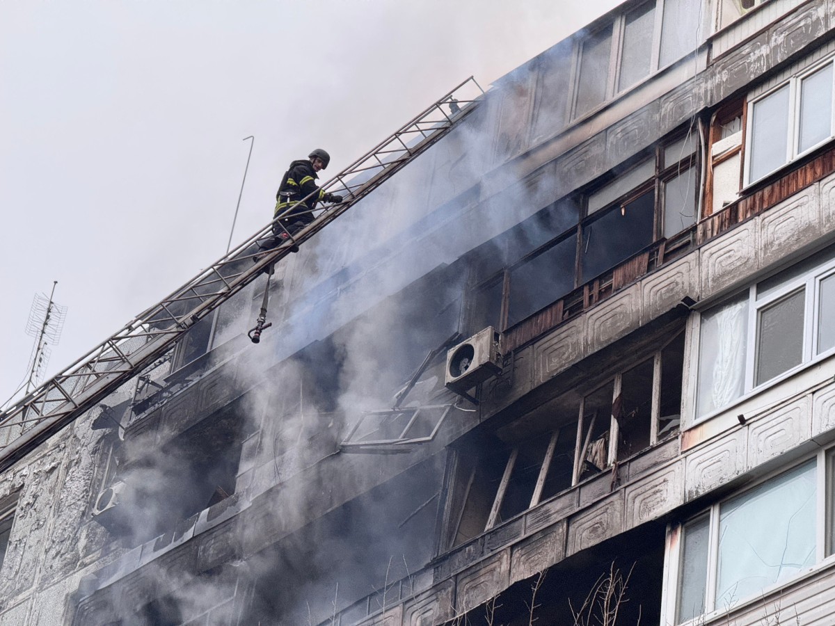 A burned out apartment building smolders as a firefighter climbs to the roof.