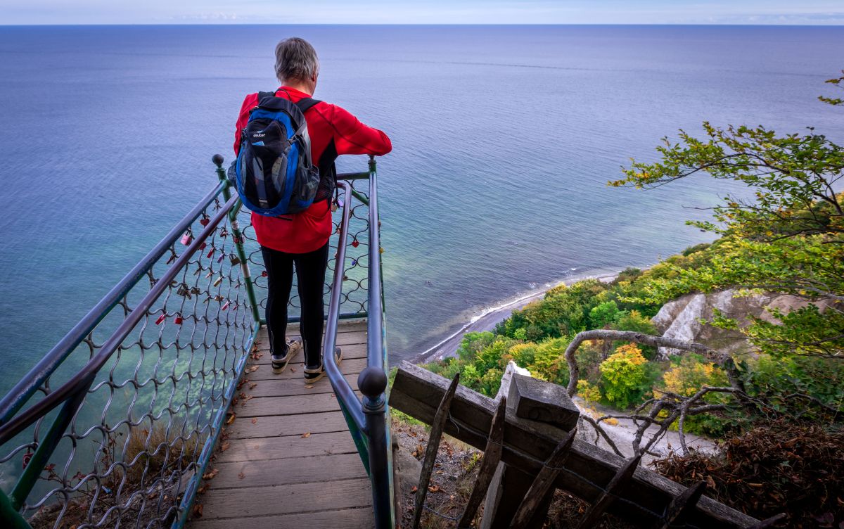 A man stands on a platform overlooking chalky cliffs and the sea below.