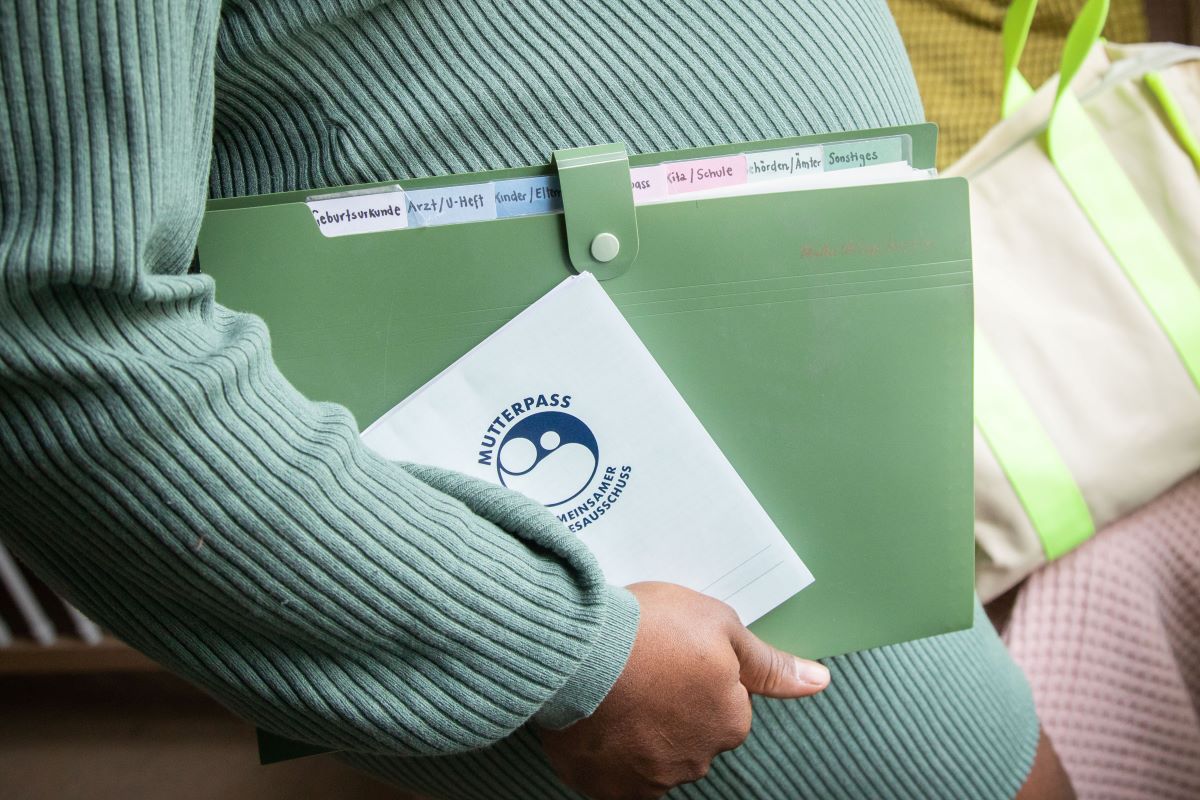 a pregnant woman holds a German Mutterpass and folder