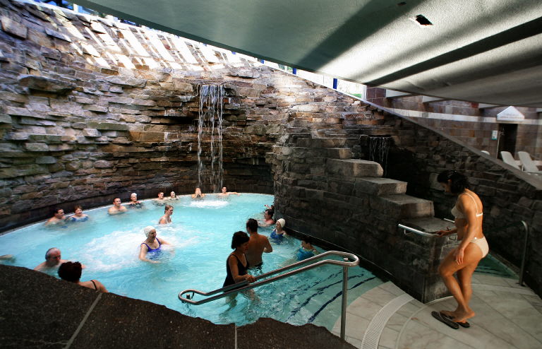 People are seen in a blue spa pool surrounded by natural rock.