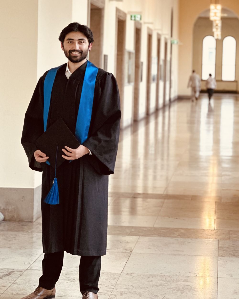 Abduallah Tayyab wears a black gown with a blue sash.