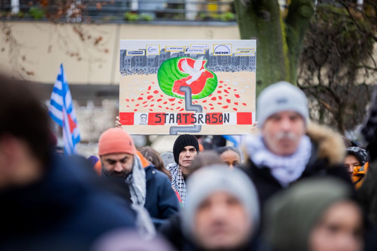 A man holds up a poster which says 'staatsrason' along with the image of a wall encircling Gaza among a sea of protestors in Berlin.