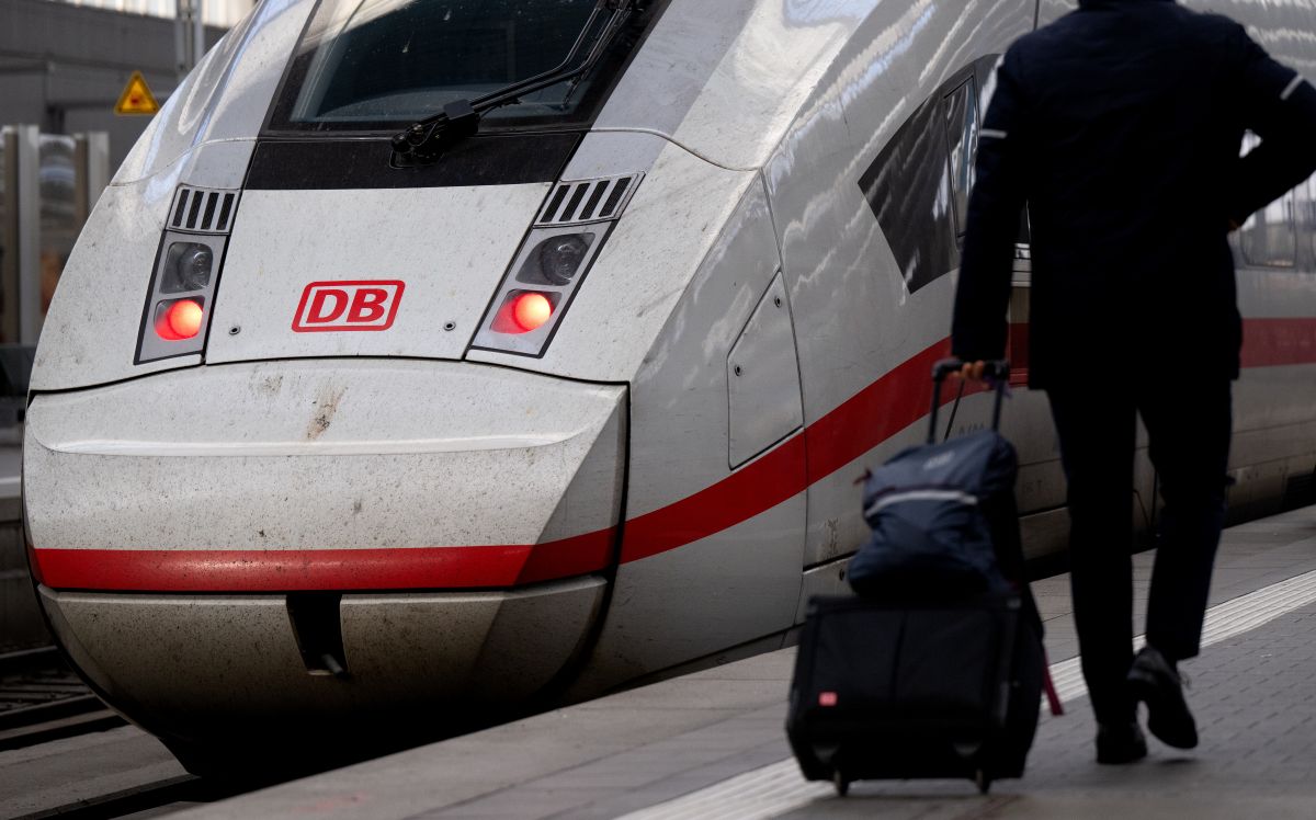 A train drivers in uniform walks toward a train on a railway station platform.