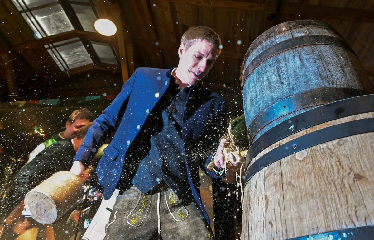 A man taps a traditional beer keg with foam spraying everywhere.