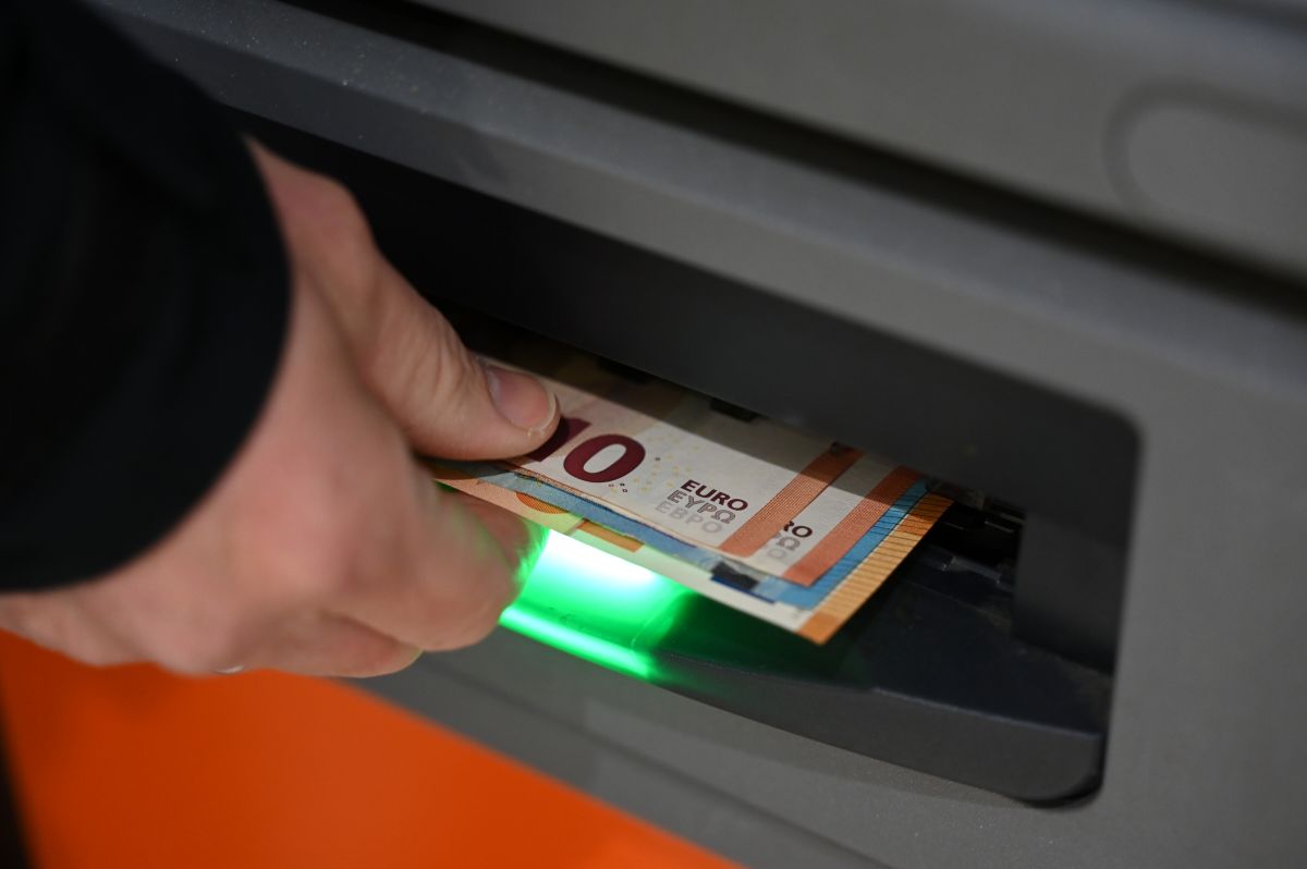 A man's hand grabs a stack of Euro notes from an atm.