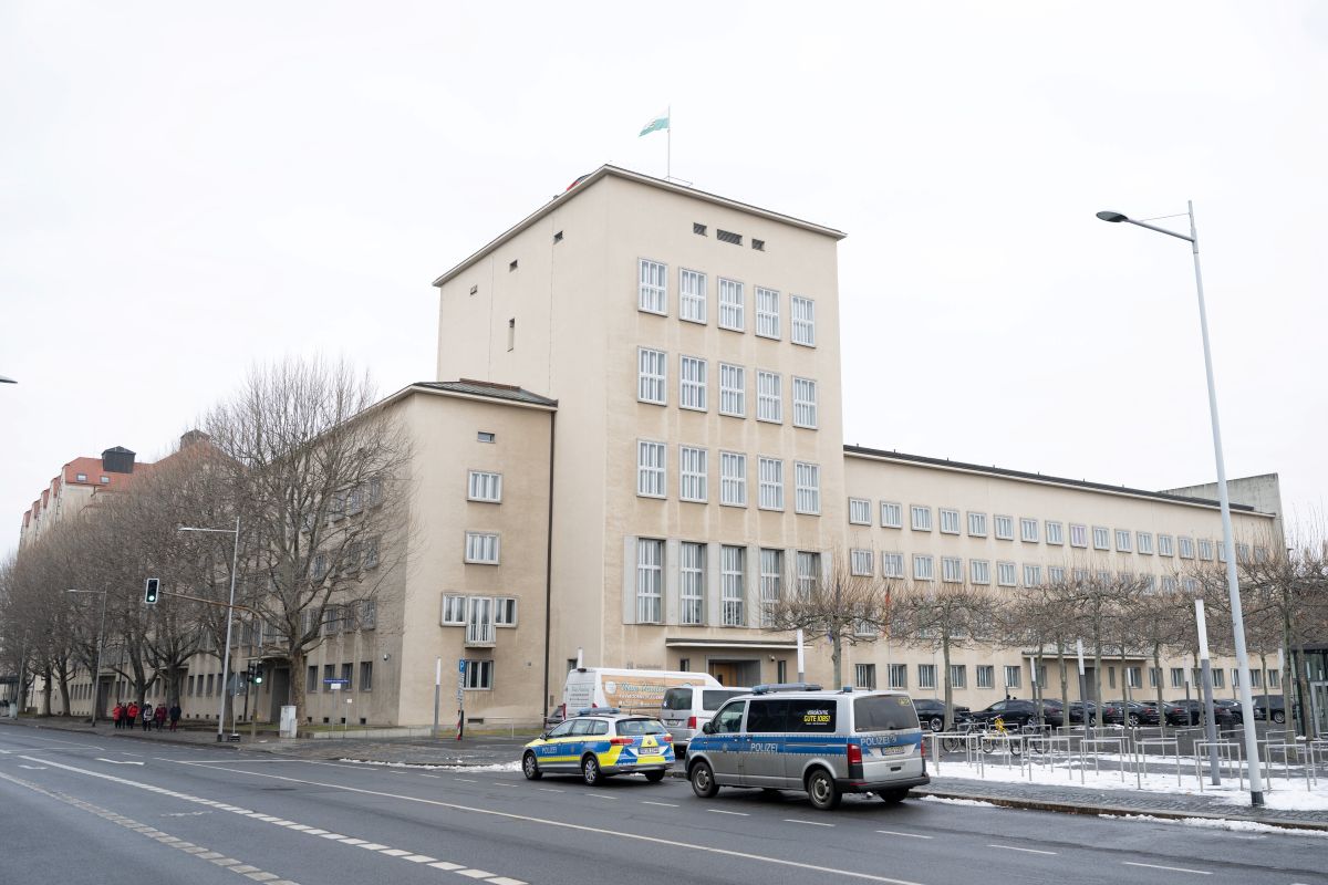 Police cars are seen in front a beigh boxy building under a grey sky in Saxony.