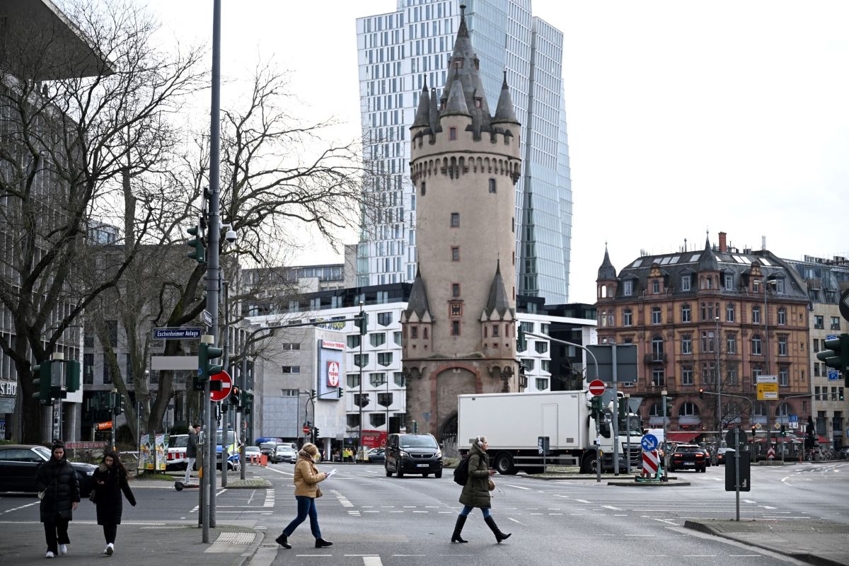 People cross the street in front of a castle tower in front of modern business buildings in Frankfurt.