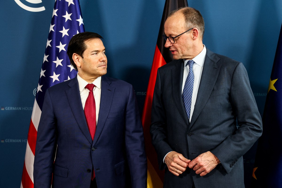 Merz and Rubio stare at each other with stern expressions in front of US and German flags.
