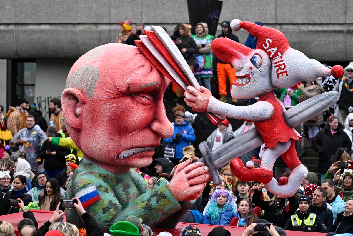An image of Putin grimmaces as a jester labeled 'satire' bashes him in the head with a paper fan.