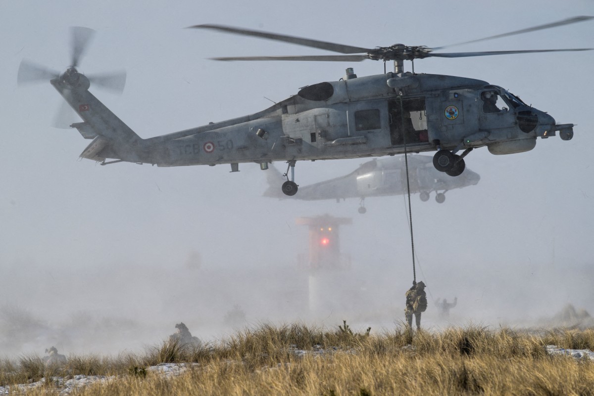 Troops dropn down form a helicopter hovering over a sandy beach.